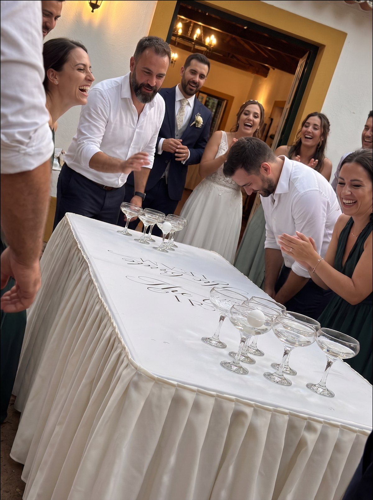 Convidados entusiasmados à volta da mesa de beer pong com taças de champanhe